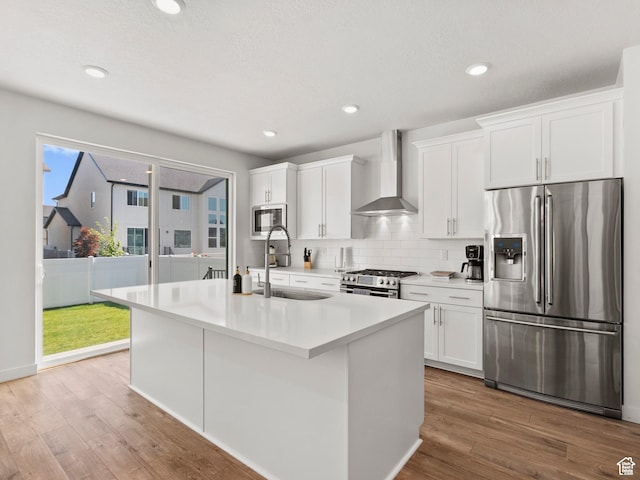 1583 W Andover Rd, South Jordan, UT 84095 - kitchen featuring appliances with stainless steel finishes, wall chimney range hood, white cabinetry, a center island with sink, and tasteful backsplash