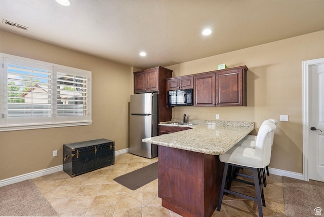 5584 N Gentle Breeze Ct, Stansbury Park, UT 84074 - kitchen with freestanding refrigerator, black microwave, a breakfast bar, recessed lighting, and light stone counters