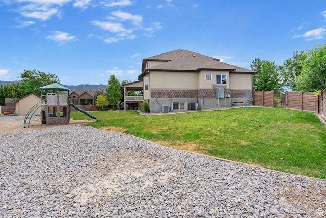 5584 N Gentle Breeze Ct, Stansbury Park, UT 84074 - rear view of house with brick siding, a playground, stucco siding, a mountain view, and a shingled roof