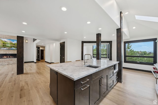 4670 Nelson Ct, Park City, UT 84098 - kitchen with a fireplace, dark brown cabinetry, light wood-style floors, a center island with sink, and recessed lighting