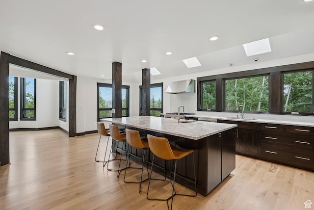 4670 Nelson Ct, Park City, UT 84098 - kitchen featuring wall chimney range hood, a skylight, a breakfast bar, a kitchen island with sink, and light stone countertops