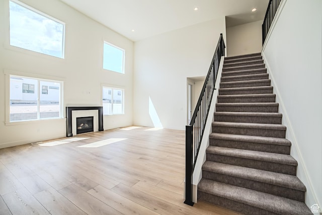 10942 S Samoa Dune Dr, South Jordan, UT 84009 - staircase featuring wood finished floors, a towering ceiling, a glass covered fireplace, and recessed lighting