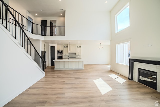 10942 S Samoa Dune Dr, South Jordan, UT 84009 - unfurnished living room featuring a high ceiling, a glass covered fireplace, light wood-type flooring, recessed lighting, and stairway