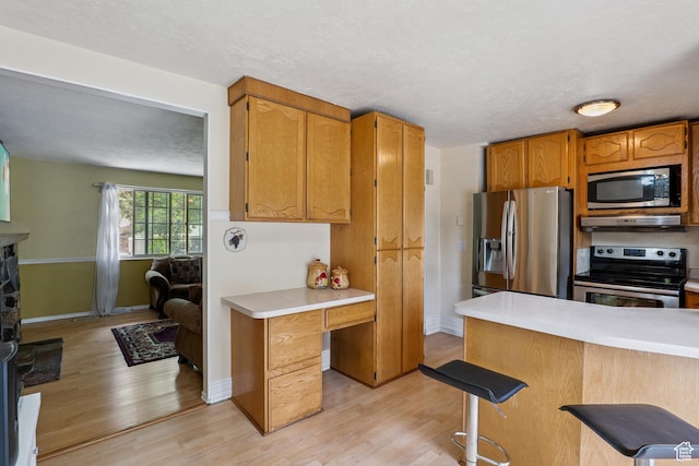 601 E Hilo St S, Sandy, UT 84070 - kitchen with appliances with stainless steel finishes, light countertops, light wood-type flooring, a breakfast bar area, and under cabinet range hood
