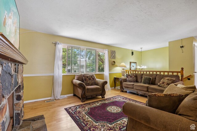 601 E Hilo St S, Sandy, UT 84070 - living room featuring a stone fireplace, light wood-style flooring, a textured ceiling, and a chandelier