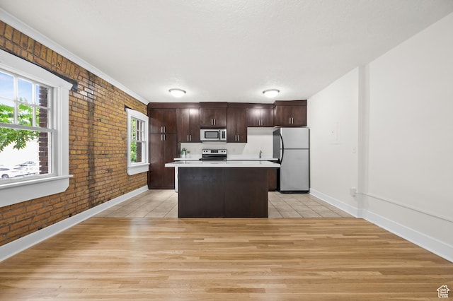 555 E 100 S Unit 303, Salt Lake City, UT 84102 - kitchen with appliances with stainless steel finishes, brick wall, a kitchen island, light countertops, and dark brown cabinets