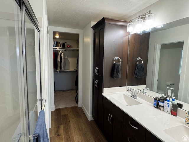 503 S Stewart Creek Cv, Washington, UT 84780 - bathroom featuring wood finished floors, a textured ceiling, double vanity, a walk in closet, and a shower with shower door