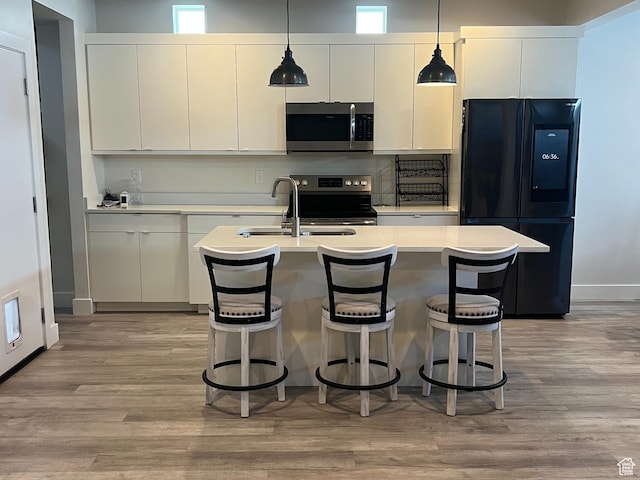 3589 S Xenon Dr W, West Valley City, UT 84119 - kitchen featuring stainless steel appliances, light countertops, light wood finished floors, white cabinetry, and an island with sink