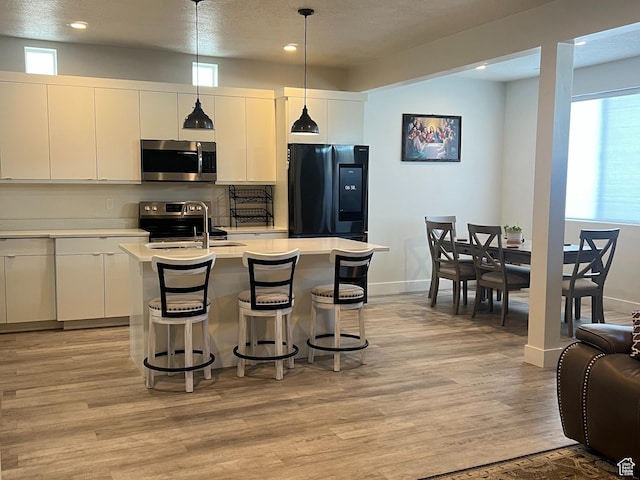 3589 S Xenon Dr W, West Valley City, UT 84119 - kitchen with appliances with stainless steel finishes, light countertops, light wood finished floors, a center island with sink, and a breakfast bar area