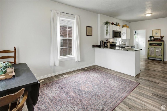 3241 Grant Ave, Ogden, UT 84401 - kitchen featuring stainless steel microwave, wood finished floors, white cabinets, and dark stone counters