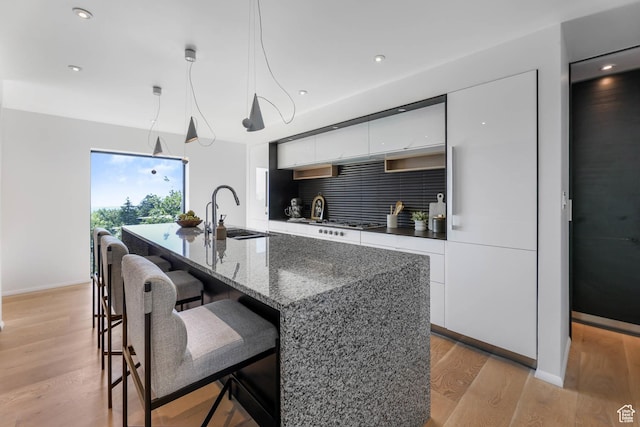 4352 S Zarahemla Dr, Salt Lake City, UT 84124 - kitchen with modern cabinets, white cabinetry, a breakfast bar, light wood-type flooring, and a kitchen island with sink