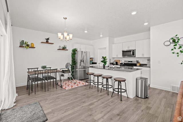 1017 S Red Cliff Dr, Santaquin, UT 84655 - kitchen featuring appliances with stainless steel finishes, a kitchen breakfast bar, dark countertops, light wood-type flooring, and a chandelier