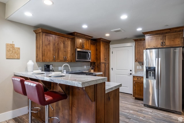 13602 N Hillclimb Ln, Kamas, UT 84036 - kitchen with stainless steel appliances, a peninsula, wood finished floors, light countertops, and a breakfast bar area