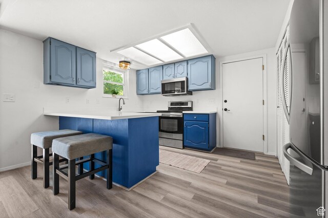 1609 E Sego Lily Dr, Sandy, UT 84092 - kitchen featuring appliances with stainless steel finishes, blue cabinets, a peninsula, a breakfast bar area, and light wood-type flooring
