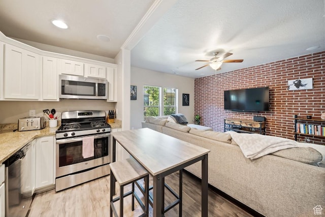 862 W Capraia Ct, Midvale, UT 84047 - kitchen with stainless steel appliances, brick wall, open floor plan, light wood-type flooring, and white cabinetry