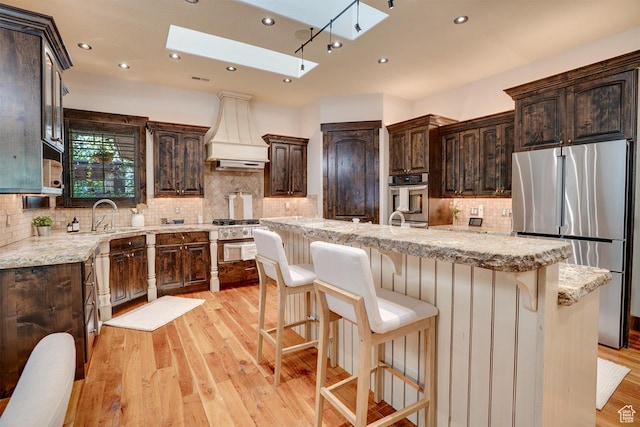 1307 N Dutch Highland Dr, Midway, UT 84049 - kitchen featuring appliances with stainless steel finishes, a skylight, custom exhaust hood, dark brown cabinets, and decorative backsplash