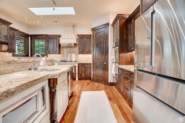 1307 N Dutch Highland Dr, Midway, UT 84049 - kitchen with appliances with stainless steel finishes, a skylight, premium range hood, light wood-type flooring, and dark brown cabinetry