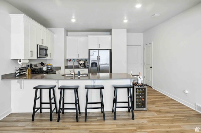 3724 W Soft Whisper Way, Herriman, UT 84096 - kitchen featuring appliances with stainless steel finishes, a peninsula, a breakfast bar area, light wood-style flooring, and white cabinetry