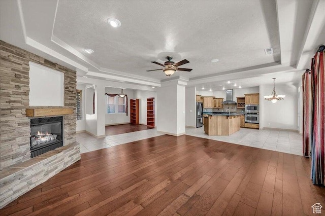 1319 W Red Butte Dr W, Washington, UT 84780 - unfurnished living room featuring a tray ceiling, a fireplace, a chandelier, a textured ceiling, and light wood-style flooring
