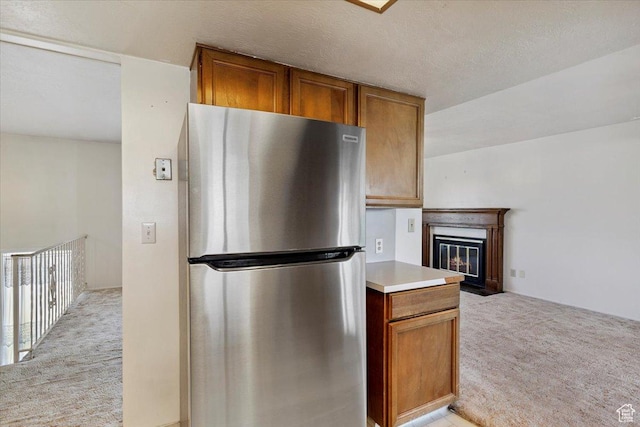 2989 W 700 S, Syracuse, UT 84075 - kitchen with freestanding refrigerator, light carpet, brown cabinetry, light countertops, and a fireplace with flush hearth