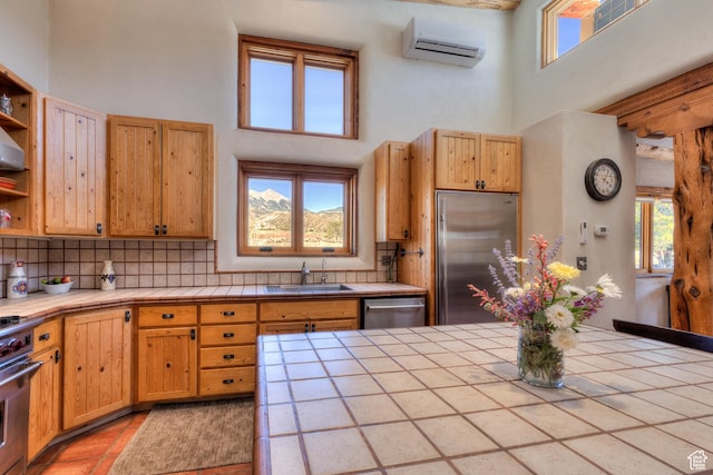 70 Desert Solitaire Rd, Moab, UT 84532 - kitchen featuring tile countertops, appliances with stainless steel finishes, a towering ceiling, a wall unit AC, and backsplash