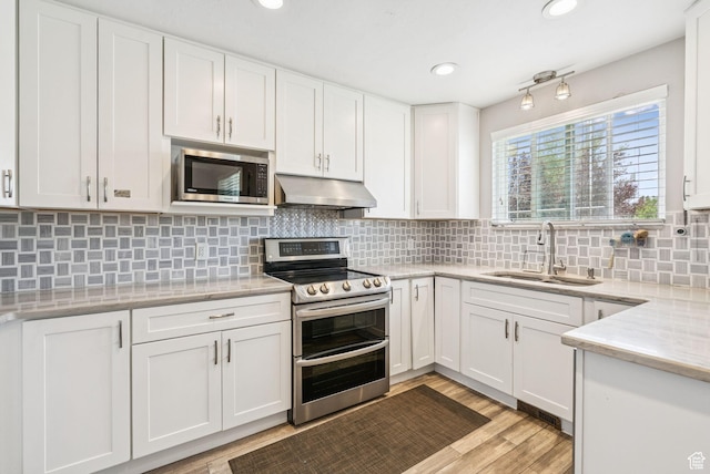 9355 S Peruvian Dr E, Sandy, UT 84093 - kitchen with appliances with stainless steel finishes, under cabinet range hood, white cabinets, light wood-style flooring, and tasteful backsplash