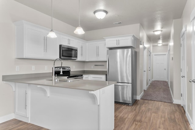 14643 S Mckellen Dr Unit D202, Herriman, UT 84096 - kitchen with stainless steel appliances, a peninsula, white cabinets, wood finished floors, and decorative light fixtures