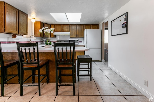 1844 Sorrento Dr, Woods Cross, UT 84087 - kitchen featuring freestanding refrigerator, under cabinet range hood, a peninsula, a skylight, and light countertops