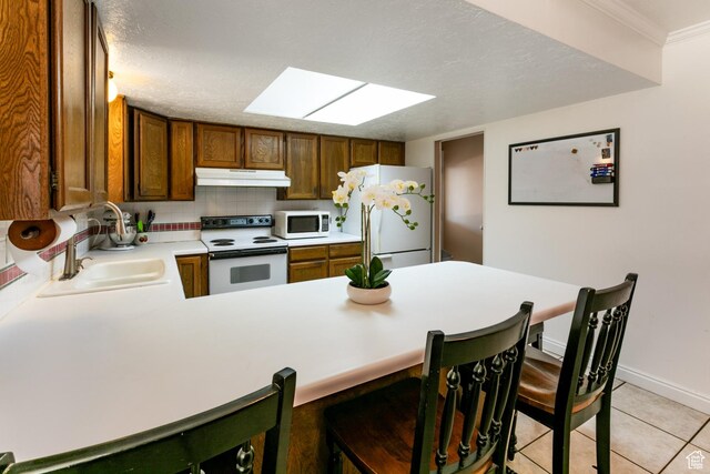 1844 Sorrento Dr, Woods Cross, UT 84087 - kitchen with white appliances, under cabinet range hood, light countertops, a skylight, and a peninsula
