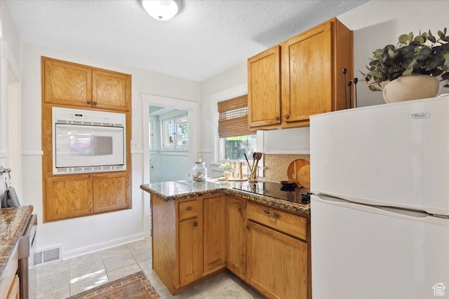 851 E Elm Ave, Salt Lake City, UT 84106 - kitchen with white appliances, dark stone counters, a peninsula, a textured ceiling, and brown cabinetry