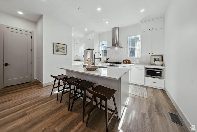 2009 E Beverly Dr S, Holladay, UT 84117 - kitchen with wall chimney range hood, wood finished floors, a center island with sink, appliances with stainless steel finishes, and recessed lighting