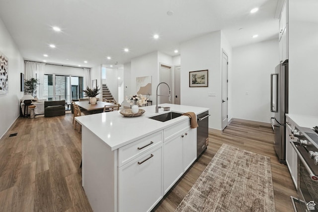 2009 E Beverly Dr S, Holladay, UT 84117 - kitchen with appliances with stainless steel finishes, white cabinets, wood finished floors, light countertops, and an island with sink
