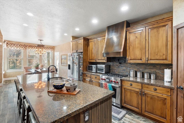 3695 S 3525 W, West Haven, UT 84401 - kitchen with stainless steel appliances, wall chimney exhaust hood, a chandelier, brown cabinetry, and a kitchen island with sink