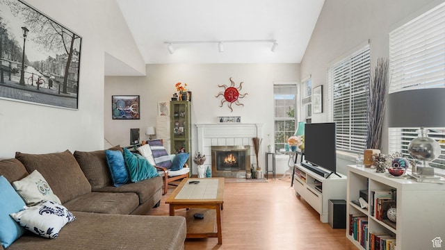 1248 E Freshman Cir, Millcreek, UT 84117 - living room featuring rail lighting, light wood-type flooring, a tiled fireplace, and vaulted ceiling
