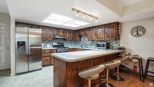 1248 E Freshman Cir, Millcreek, UT 84117 - kitchen with appliances with stainless steel finishes, under cabinet range hood, light countertops, a peninsula, and decorative backsplash