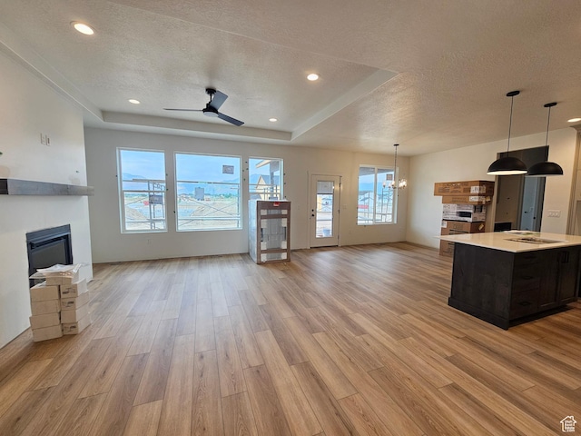 1768 S 3875 W Unit 227, Taylor, UT 84401 - unfurnished living room featuring a textured ceiling, a glass covered fireplace, light wood-style flooring, a ceiling fan, and a tray ceiling