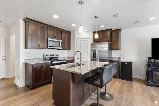 1152 S 800 W, Spanish Fork, UT 84660 - kitchen with appliances with stainless steel finishes, dark brown cabinetry, light wood-style flooring, a breakfast bar area, and a textured ceiling