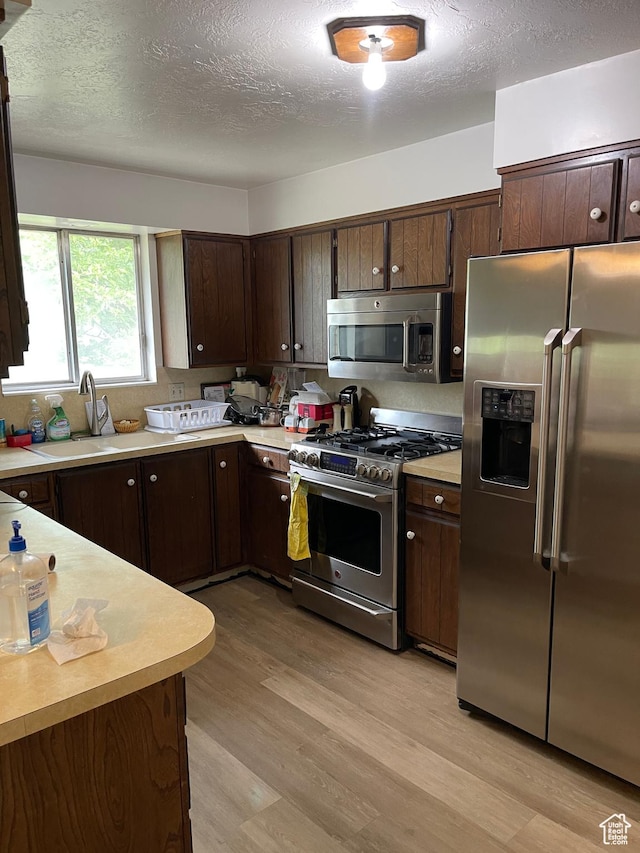 1692 W 300 N, West Point, UT 84015 - kitchen with stainless steel appliances, light countertops, light wood-type flooring, dark brown cabinetry, and a textured ceiling