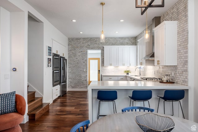 334 N C St, Salt Lake City, UT 84103 - kitchen with dark wood finished floors, stainless steel appliances, a peninsula, wall chimney range hood, and light countertops