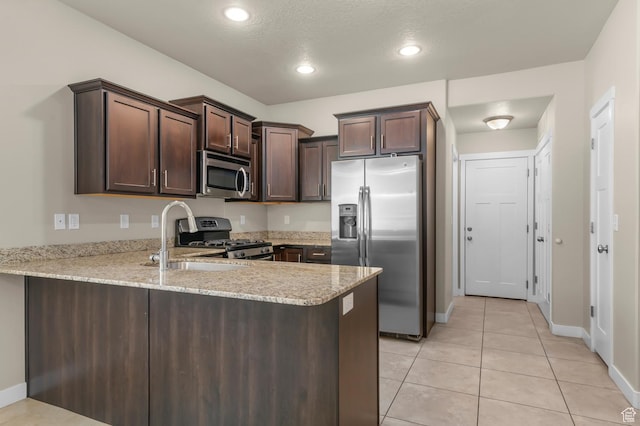 1012 W Willow Wind Dr, Farmington, UT 84025 - kitchen featuring appliances with stainless steel finishes, a peninsula, dark brown cabinets, light tile patterned flooring, and light stone countertops