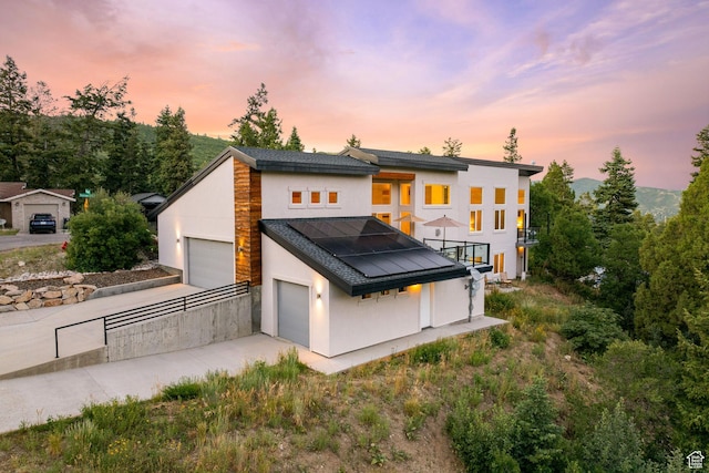 249 S Parkview Dr E, Park City, UT 84098 - back of property at dusk with solar panels, stucco siding, driveway, a balcony, and a garage