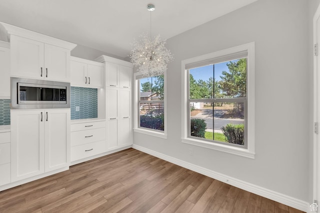 960 E 6740 S, Midvale, UT 84047 - kitchen featuring stainless steel microwave, light wood-type flooring, decorative backsplash, white cabinetry, and a chandelier