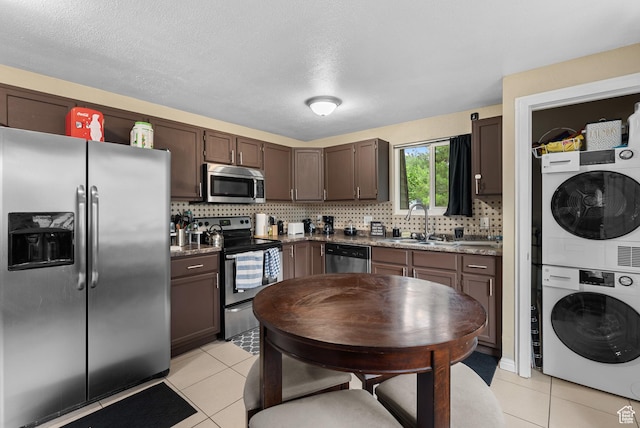1191 W 4300 S Unit 15A, Taylorsville, UT 84123 - kitchen featuring stainless steel appliances, stacked washing machine and dryer, light tile patterned floors, backsplash, and dark brown cabinets