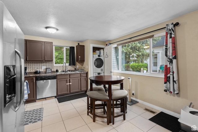 1191 W 4300 S Unit 15A, Taylorsville, UT 84123 - kitchen with appliances with stainless steel finishes, stacked washing machine and dryer, tasteful backsplash, light tile patterned floors, and dark brown cabinetry