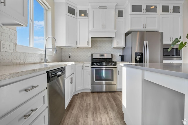 4982 N Goosefoot Dr Unit 51, Eagle Mountain, UT 84005 - kitchen featuring appliances with stainless steel finishes, light wood-style floors, white cabinetry, backsplash, and glass insert cabinets