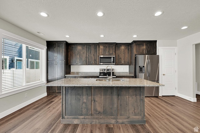 2782 W 4140 S Unit 246, Roy, UT 84067 - kitchen featuring appliances with stainless steel finishes, a kitchen island with sink, dark wood-style floors, light stone countertops, and a textured ceiling