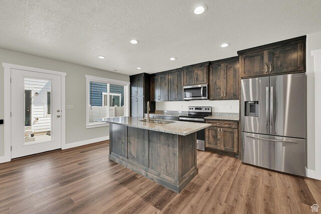 2782 W 4140 S Unit 246, Roy, UT 84067 - kitchen featuring stainless steel appliances, wood finished floors, a kitchen island with sink, a textured ceiling, and light stone countertops