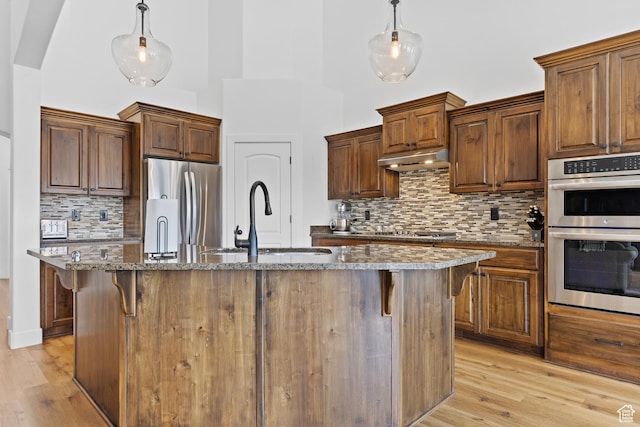 4323 W 2650th Cir S, Hurricane, UT 84737 - kitchen with appliances with stainless steel finishes, dark stone countertops, light wood-style flooring, decorative backsplash, and a towering ceiling