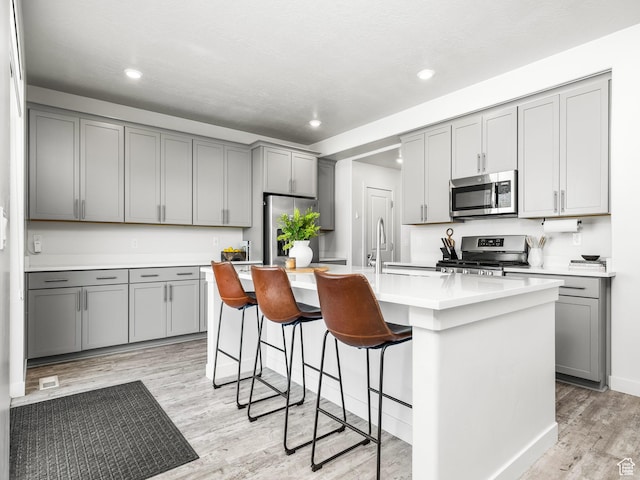 1911 N Lemongrass Dr, Saratoga Springs, UT 84045 - kitchen with stainless steel appliances, gray cabinetry, light wood-style flooring, an island with sink, and recessed lighting