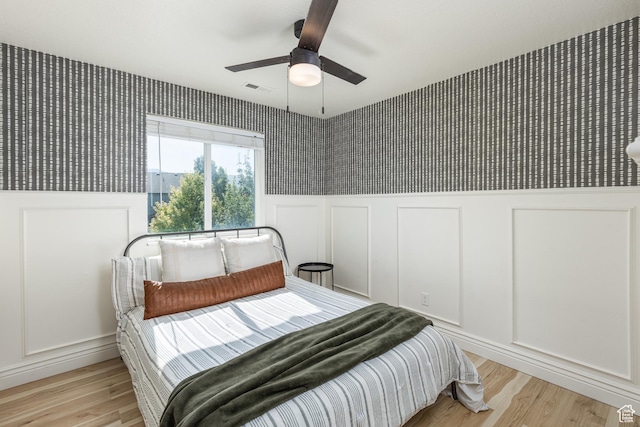 1012 N Cambria Dr, North Salt Lake, UT 84054 - bedroom with a decorative wall, light wood-type flooring, ceiling fan, wainscoting, and wallpapered walls